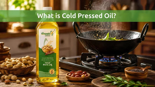 Sri Saraswathi Organics cold pressed groundnut oil bottle in a kitchen with a traditional iron kadai tempering mustard seeds and curry leaves